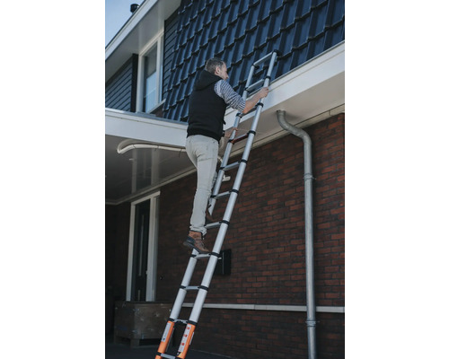 Man klättrar på en teleskopisk stege mot ett hus