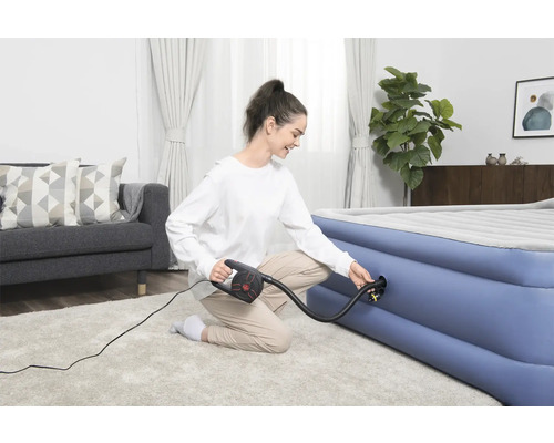 Kvinna pumpar upp luftmadrass med en elektrisk pump i ett ljust vardagsrum