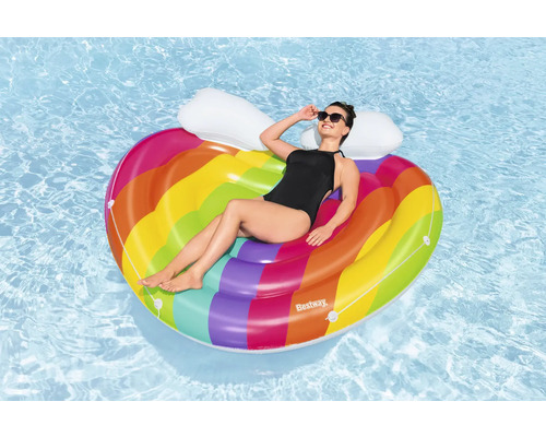 Kvinna kopplar av på en regnbågsfärgad, hjärtformad luftmadrass i vattnet.