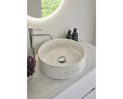 Rund tvättställsskål i terrazzo med armatur och handlotion på en bänkskiva