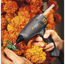 Steinel limpistol applicerar lim på en grön plastskiva, omgiven av orange blommor.