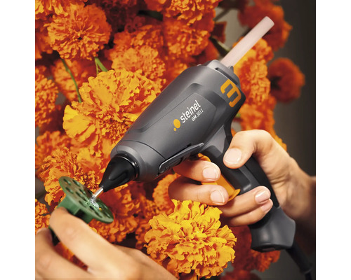 Steinel limpistol applicerar lim på en grön plastskiva, omgiven av orange blommor.