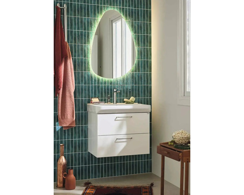 Badrum med belyst spegel, tvättställsskåp och blandare framför en grön vägg