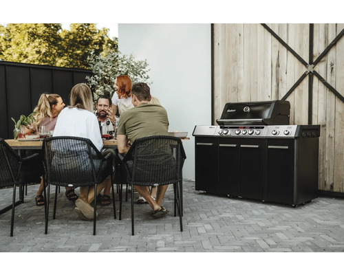 En grupp människor sitter vid ett bord bredvid en Enders gasolgrill i trädgården.