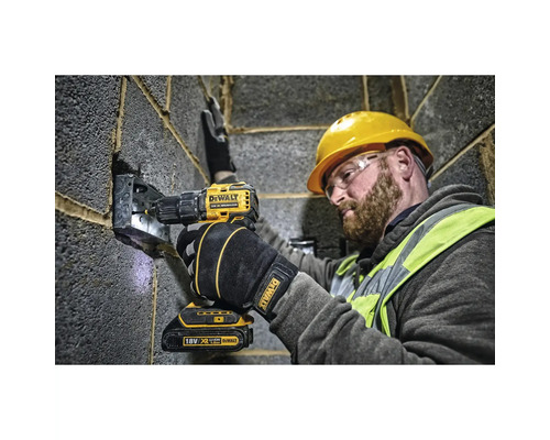 En byggnadsarbetare använder en gul DeWalt sladdlös skruvdragare för att fästa en metallbit på en grå tegelvägg.