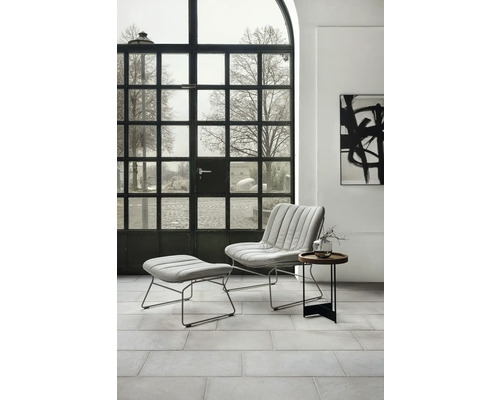 Vardagsrum i modern stil med fåtölj, fotpall och sidobord framför ett spröjsat fönster.