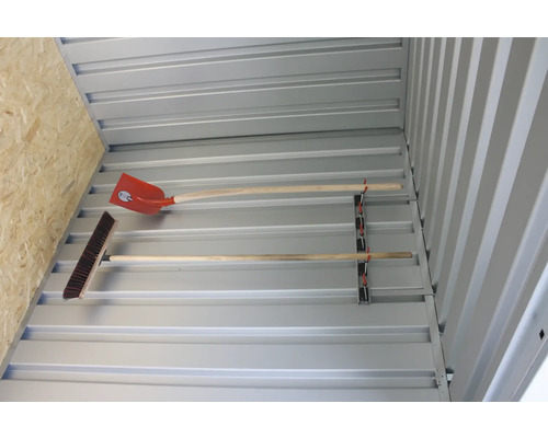 Interiörbild av ett trädgårdsskjul med verktygshållare där en spade och en kvast är fästa