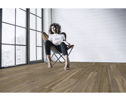 Vardagsrum med trägolv och en kvinna som sitter i en fåtölj.