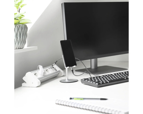 Arbetsplats med grenuttag, bildskärm, tangentbord, telefonhållare med smartphone, anteckningsblock och växt