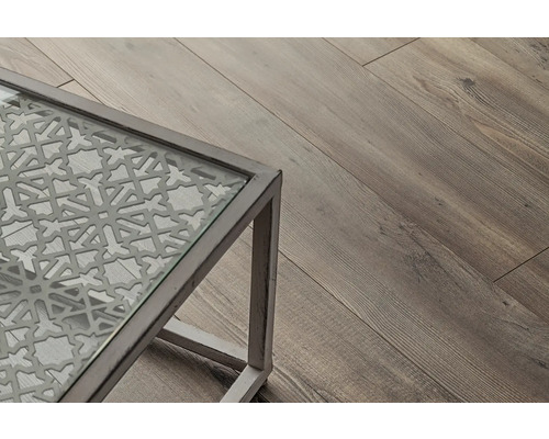 Detaljvy av ett bord med glasskiva och dekorativt mönster, bredvid ett trägolv.