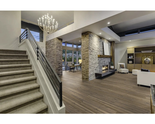 Interiörbild av ett vardagsrum med trappa, öppen spis, trägolv och belysning