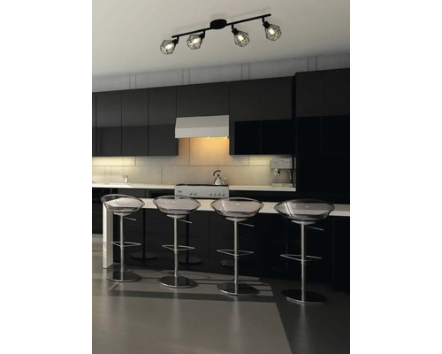 Modernt kök med svart köksinredning, transparenta barstolar och en svart taklampa med fyra spotlights.