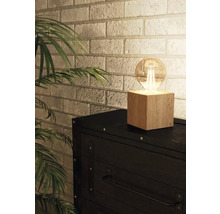 Bordslampa med träfot och glödlampa på en byrå framför en tegelvägg