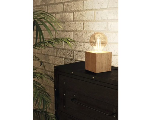 Bordslampa med träfot och glödlampa på en byrå framför en tegelvägg