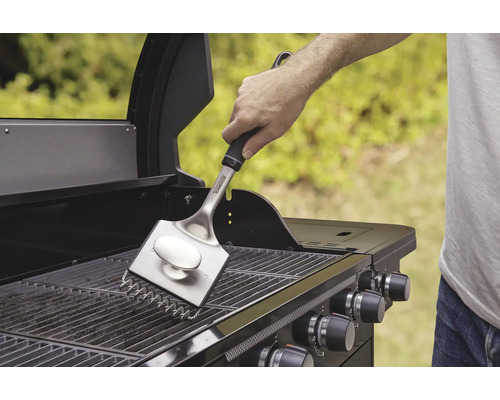 En person rengör grillgallret med en grillborste.