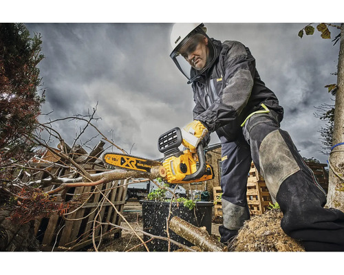 En man med skyddsutrustning använder en DeWalt motorsåg för att beskära grenar.
