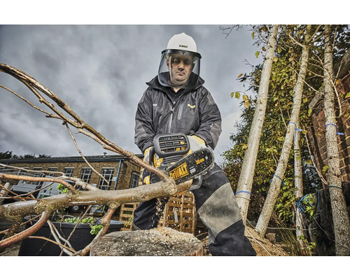 En person med skyddskläder och hjälm sågar av en gren med en batteridriven motorsåg. Träd syns i bakgrunden.