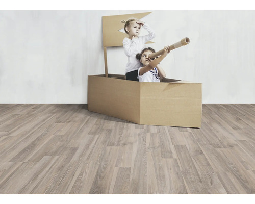Två barn leker i en kartongbåt på ett trägolv.