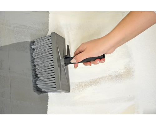 En person målar en vägg med en flat pensel.