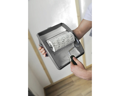 Person håller en färgroller och ett färgtråg med färg för målning