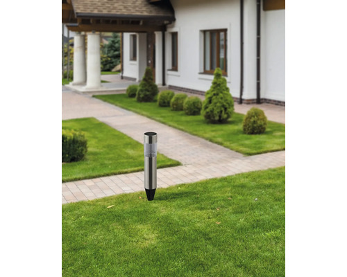 Trädgård med en gångvägsbelysning i rostfritt stål i gräsmattan framför ett hus